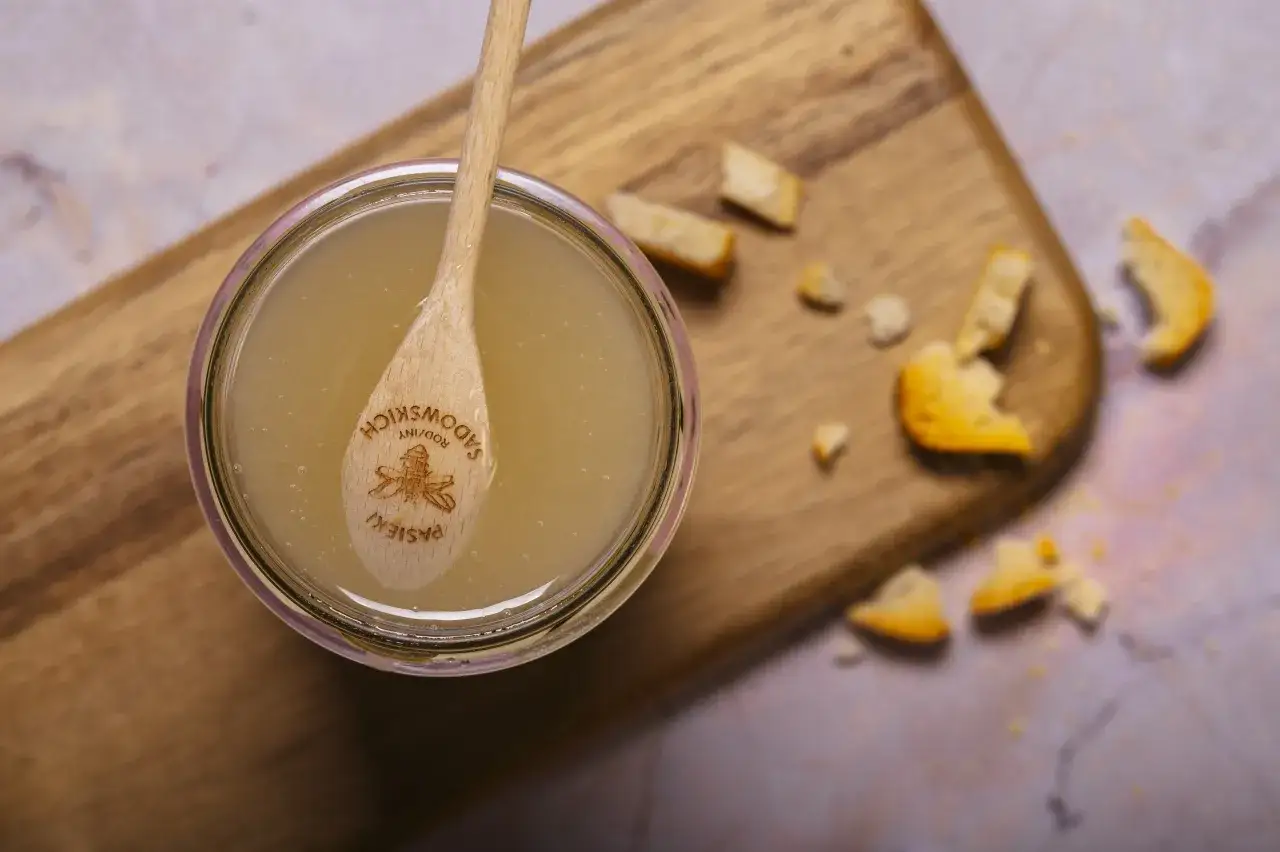 Słoik miodu z drewnianą łyżką z pszczołą. Czy mi&oacute;d jest wegański? To pytanie nurtuje wielu.