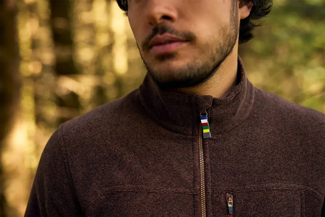 Mężczyzna w brązowym polarze z kolorową naszywką na suwaku. Idealny na chłodne dni, ten polar to świetny wyb&oacute;r.