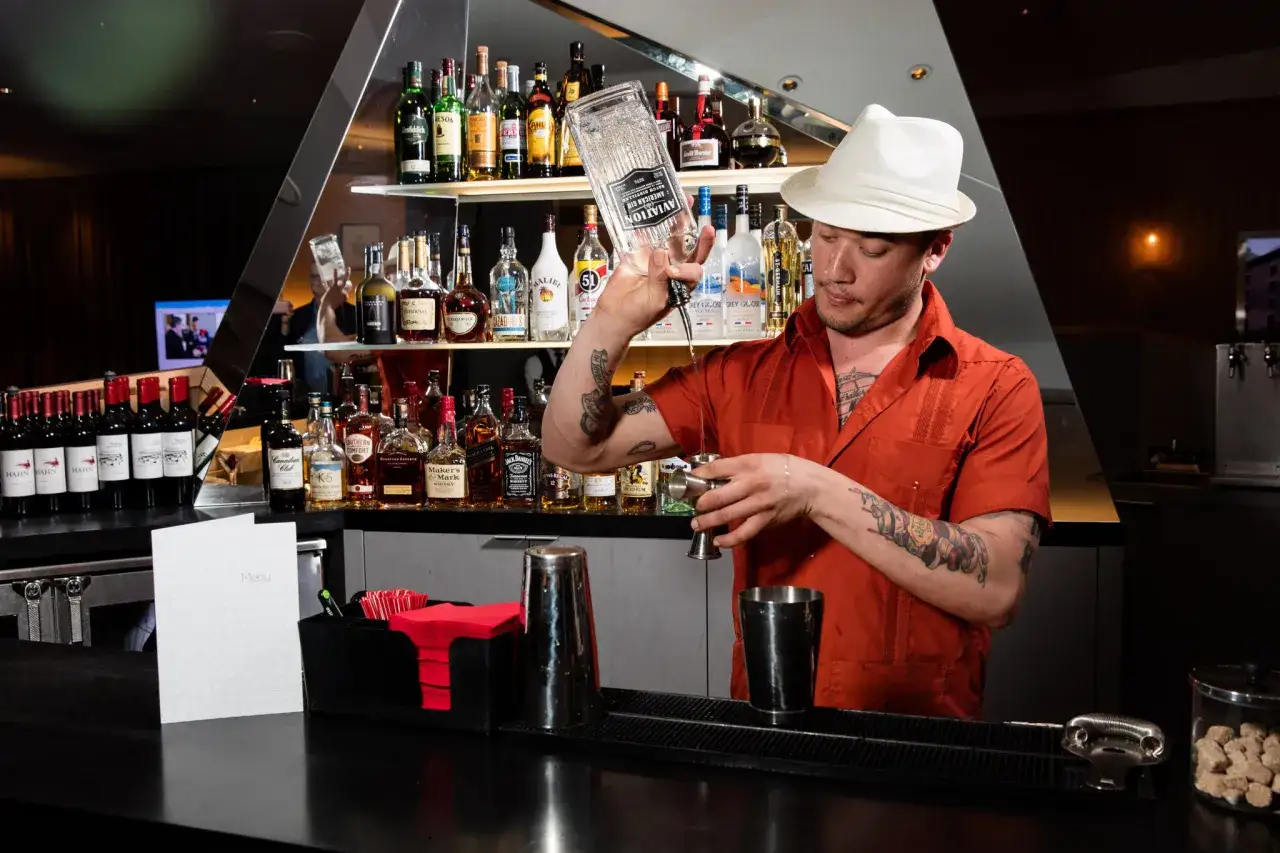 Barman w białym kapeluszu nalewa alkohol. Czy na lotnisku można pić alkohol? Tak, w barach lotniskowych.