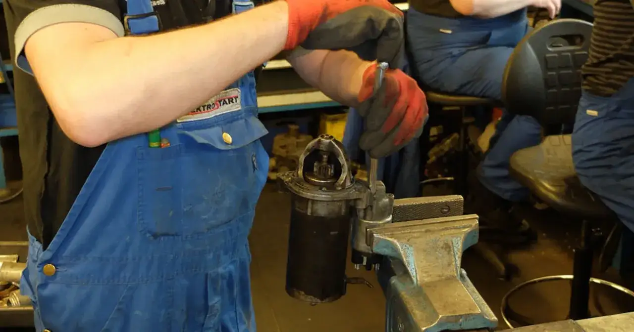 Mechanik w niebieskim kombinezonie naprawia rozrusznik. Słychać, jak przekaźnik cyka, ale rozrusznik nie kręci.