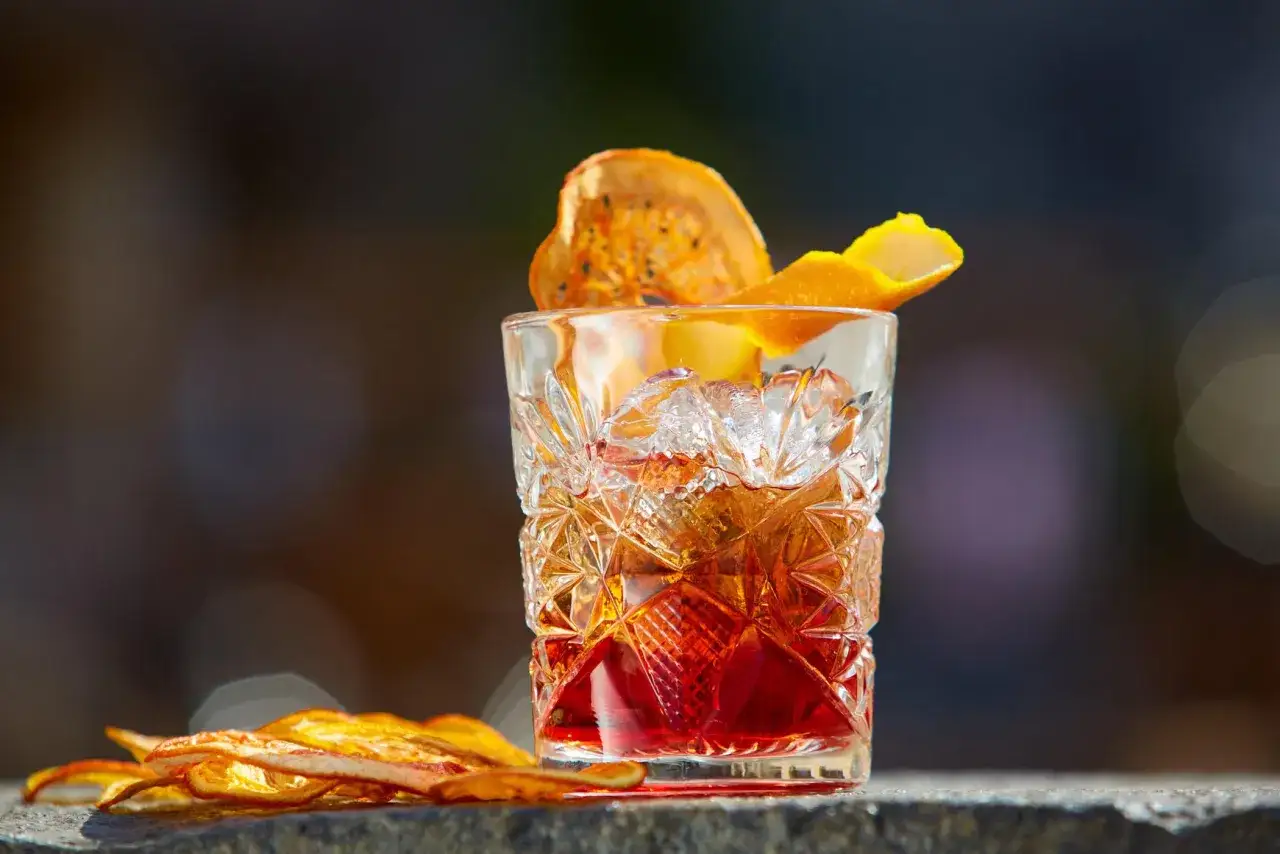 Szklanka z lodem i czerwonym drinkiem, ozdobiona skórką pomarańczy i suszonym owocem. Klasyczny, old fashioned drink.