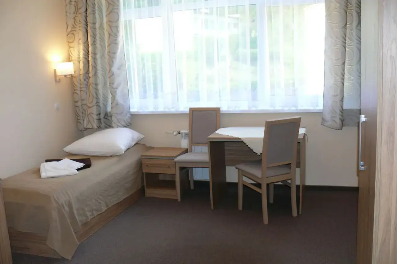 Pok&oacute;j w sanatorium Leśnik Drzewiarz Krynica Zdr&oacute;j, ul. Podg&oacute;rna 1. Ł&oacute;żko, stolik, krzesła i okno.