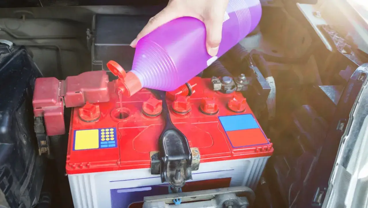 Ręka wlewa fioletowy płyn w akumulatorze samochodowym, uzupełniając elektrolit.