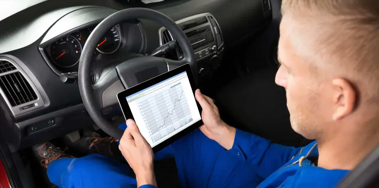 Mechanik analizuje wykresy na tablecie, szukając objaw&oacute;w zużytego płynu wspomagania kierownicy.