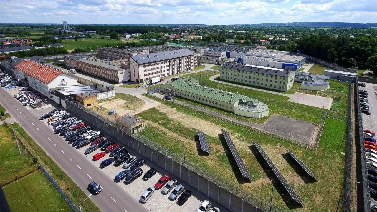 Widok z lotu ptaka na kompleks budynków otoczony murem i ogrodzeniem z drutem kolczastym. To miejsce, gdzie realizuje się cele penitencjarne.