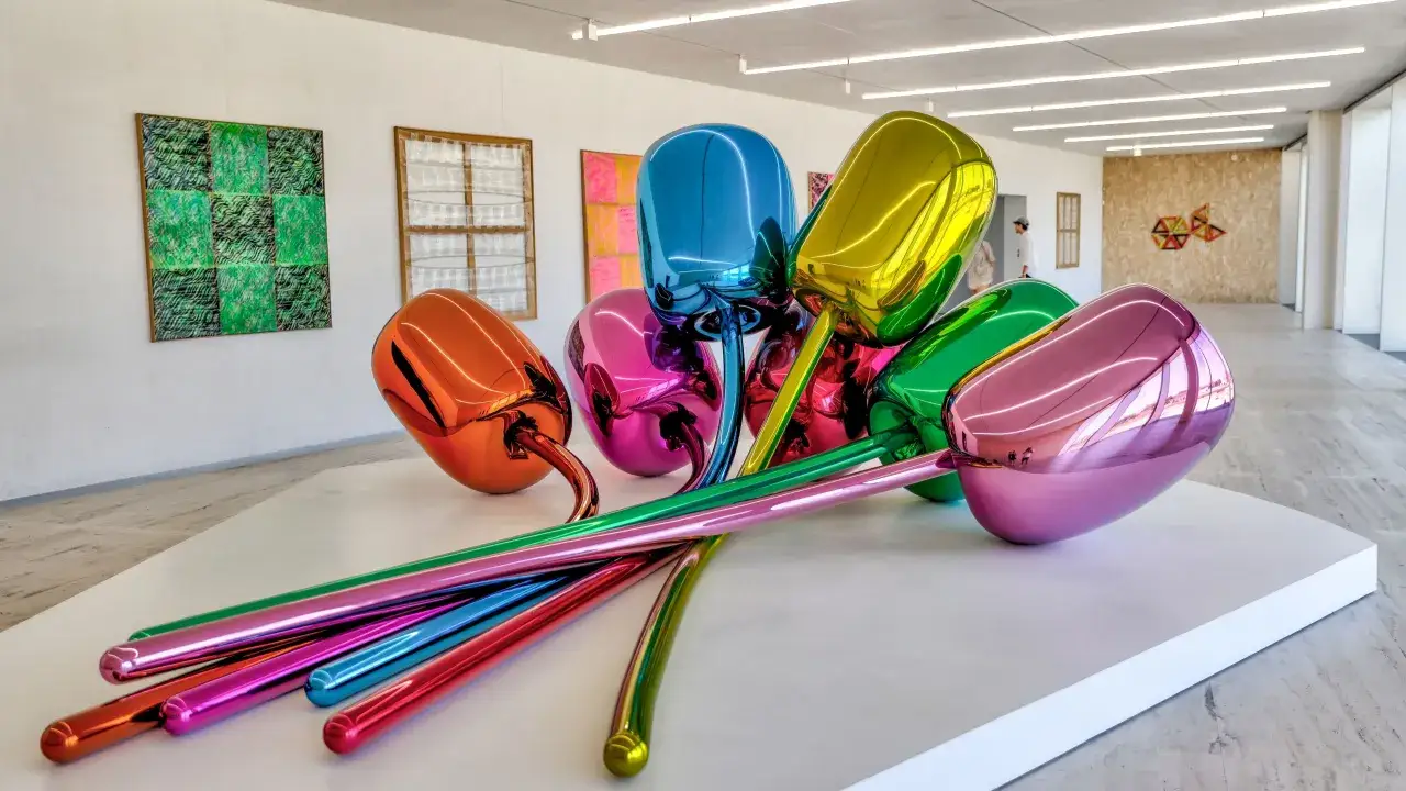 Błyszczące, metaliczne rzeźby pop art w kształcie tulipanów w jaskrawych kolorach: różowym, niebieskim, zielonym, żółtym i pomarańczowym.