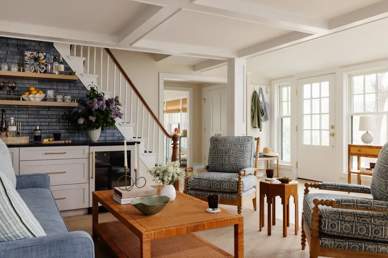 Przytulny salon z niebieską sofą, fotelami w geometryczne wzory i rattanowym stolikiem kawowym. Dobry design, kt&oacute;ry zachęca do relaksu.