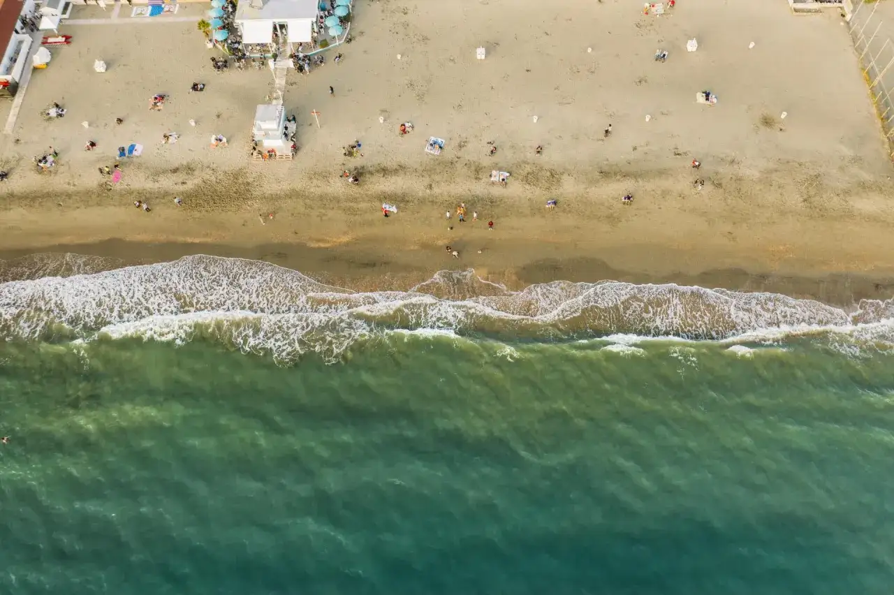 Widok z lotu ptaka na plażę, gdzie z Rzymu nad morze przybyli ludzie, by odpocząć. Fale obmywają brzeg.