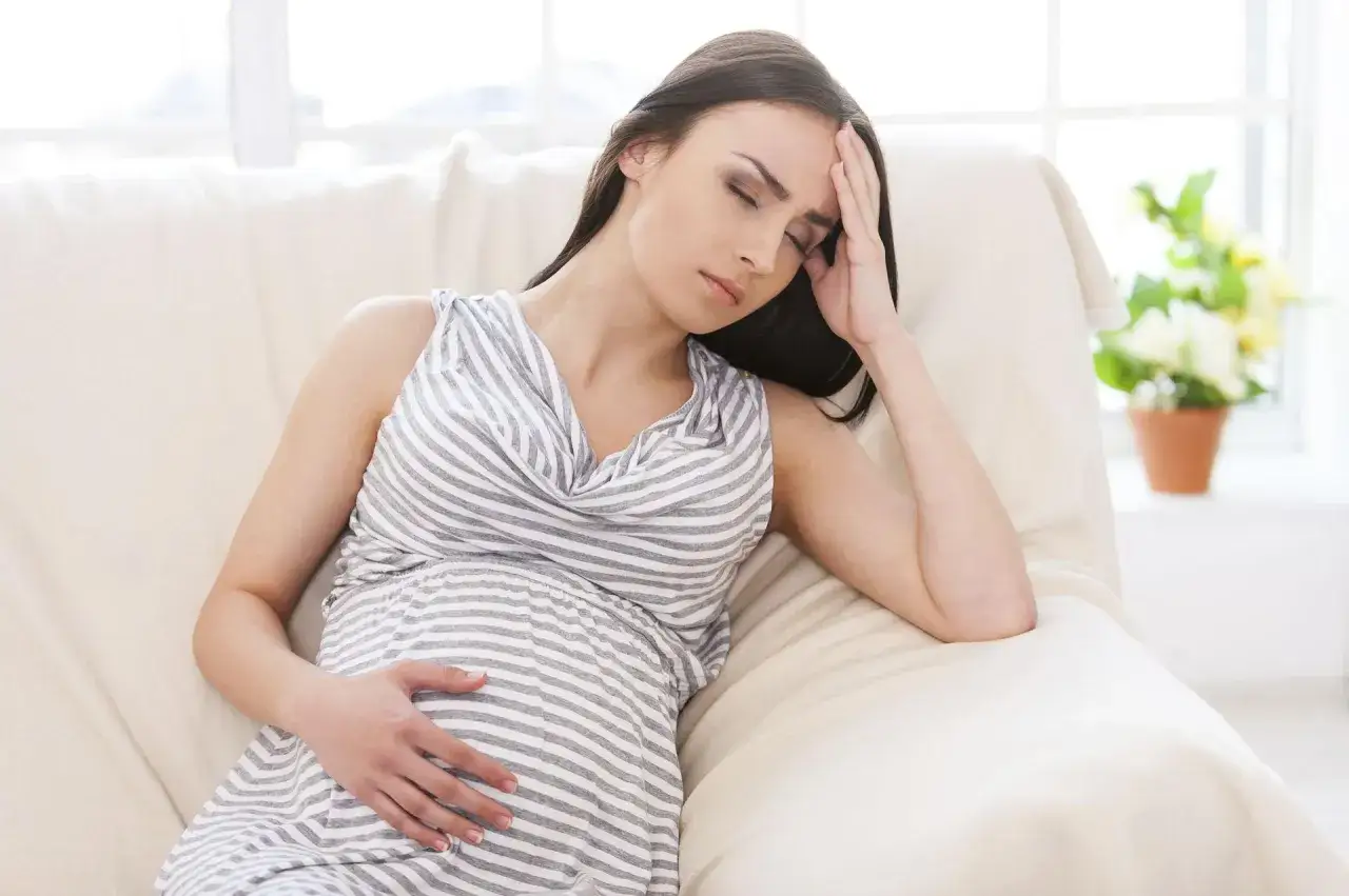 Kobieta w ciąży z ręką na skroni, zastanawia się, czy ból głowy może być objawem ciąży.