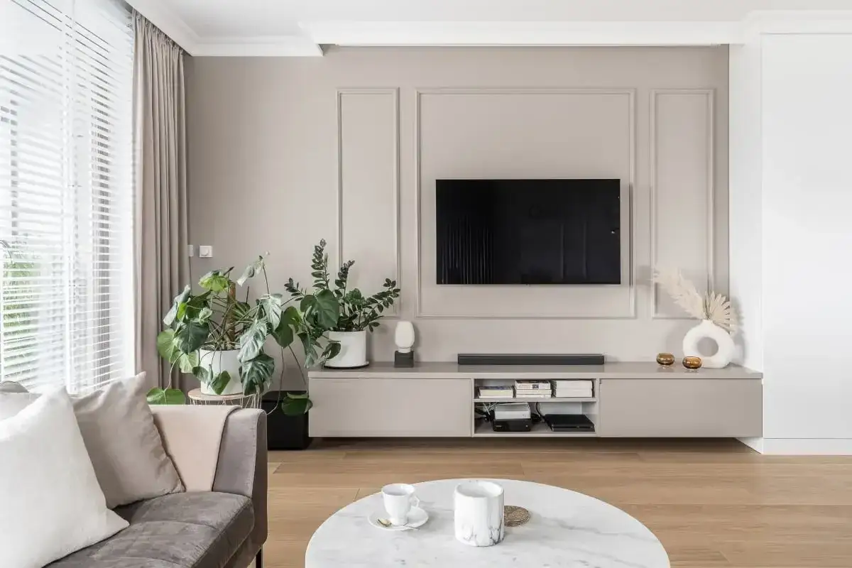 Elegancka ściana TV glamour z nowoczesnym telewizorem, minimalistyczną szafką i roślinami tworzy przytulną atmosferę.