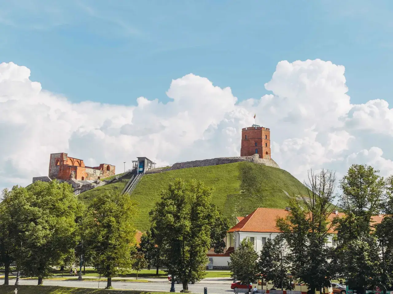 Wzg&oacute;rze Giedymina z wieżą i ruinami zamku na tle błękitnego nieba z chmurami.