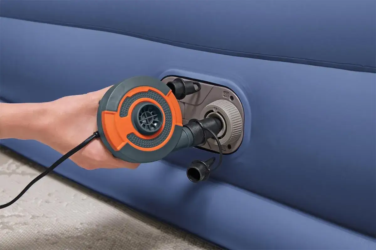 Ręka trzyma pompkę, podłączoną do zaworu materaca. Prosty sposób, jak napompować materac z wbudowaną pompką.