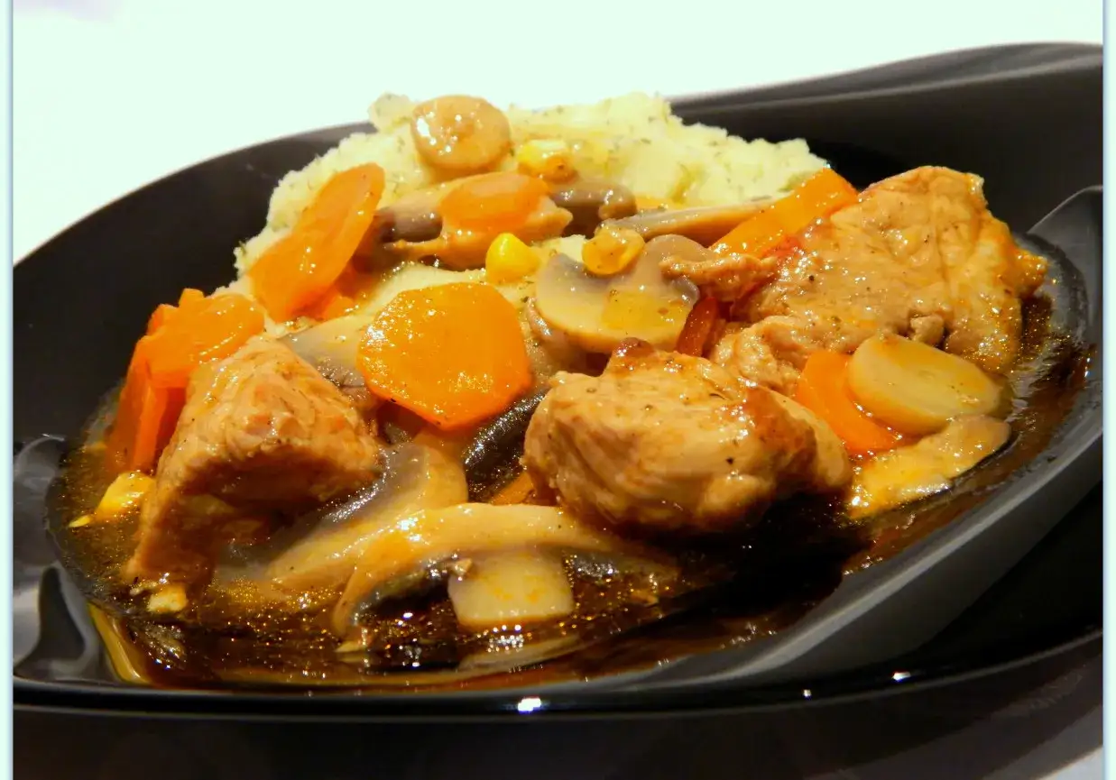 Pyszne danie z biodrówki wieprzowej na obiad: kawałki mięsa, marchewka, pieczarki i kukurydza w sosie, podane z puree ziemniaczanym.