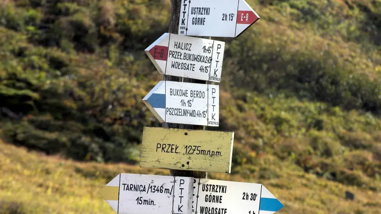 Znaki szlaku turystycznego w g&oacute;rach, w tym czarny szlak, wskazują drogę. Na tabliczkach nazwy miejscowości i czasy przejścia.