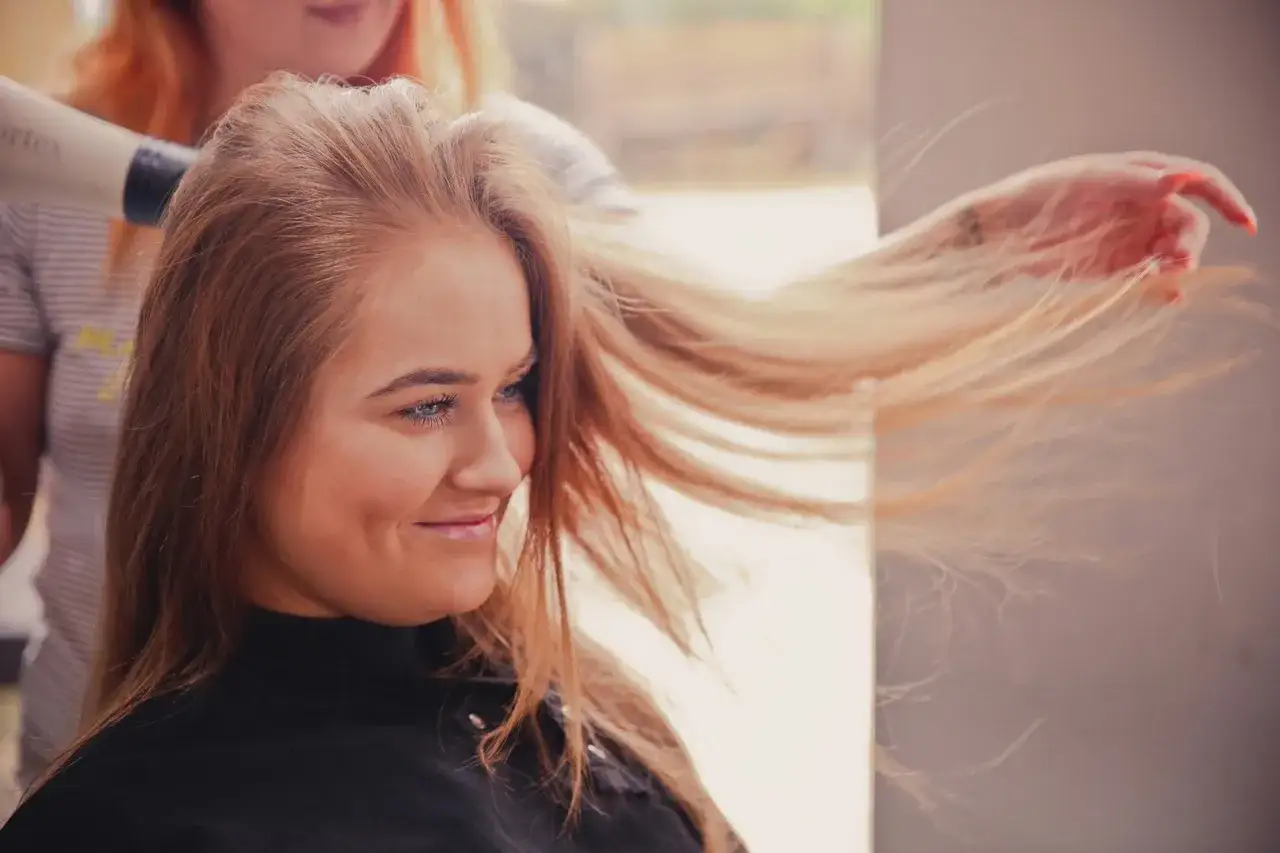 Uśmiechnięta kobieta z blond włosami, które lekka trwała unosząca włosy, suszy fryzjerka.