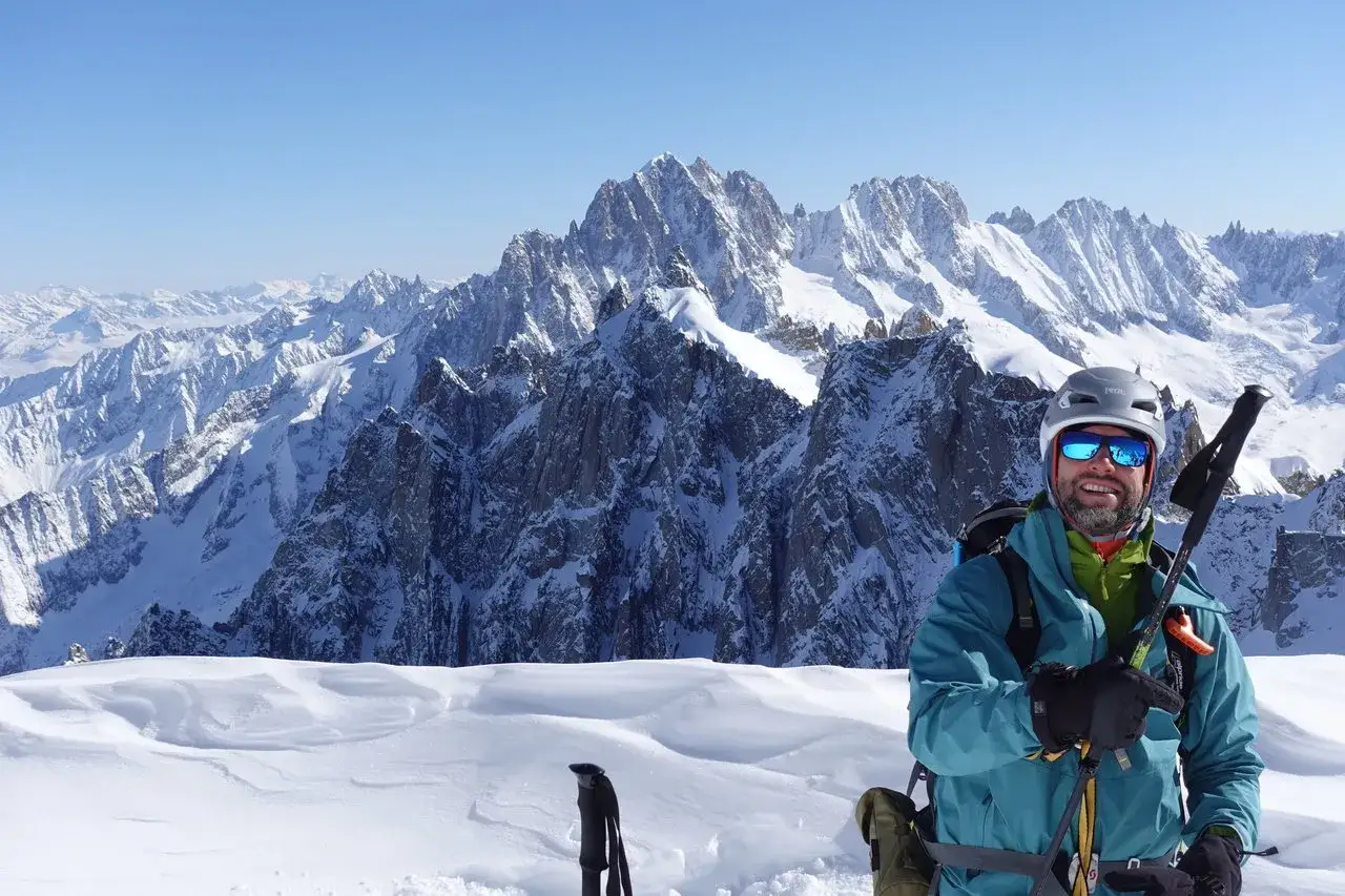 Uśmiechnięty narciarz w kasku i goglach na tle majestatycznego Mont Blanc. Śnieżne szczyty Alp rozciągają się w oddali.
