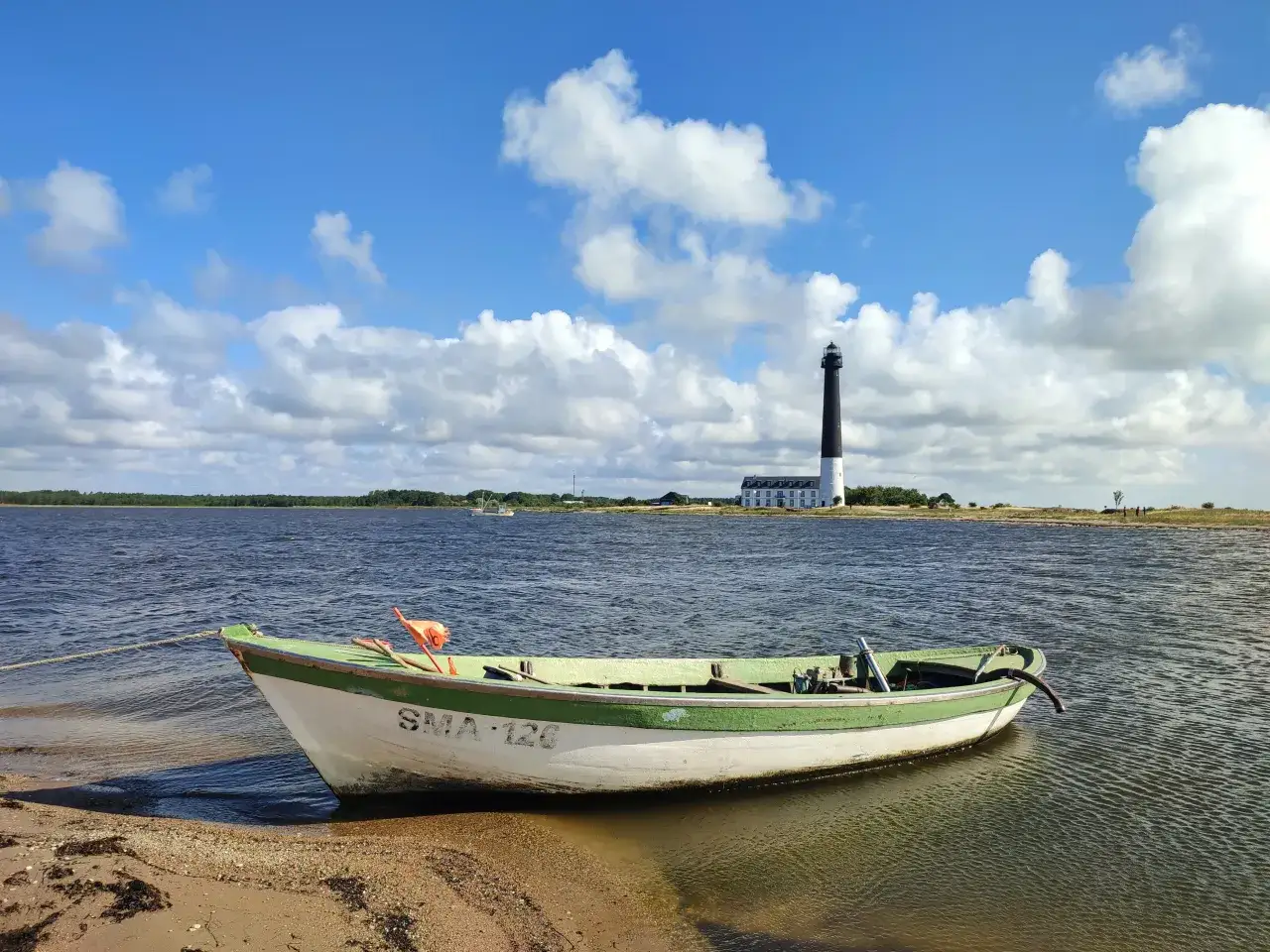 Łódź przy brzegu, latarnia morska w oddali. To widok z Estonii, która ma dostęp do morza.