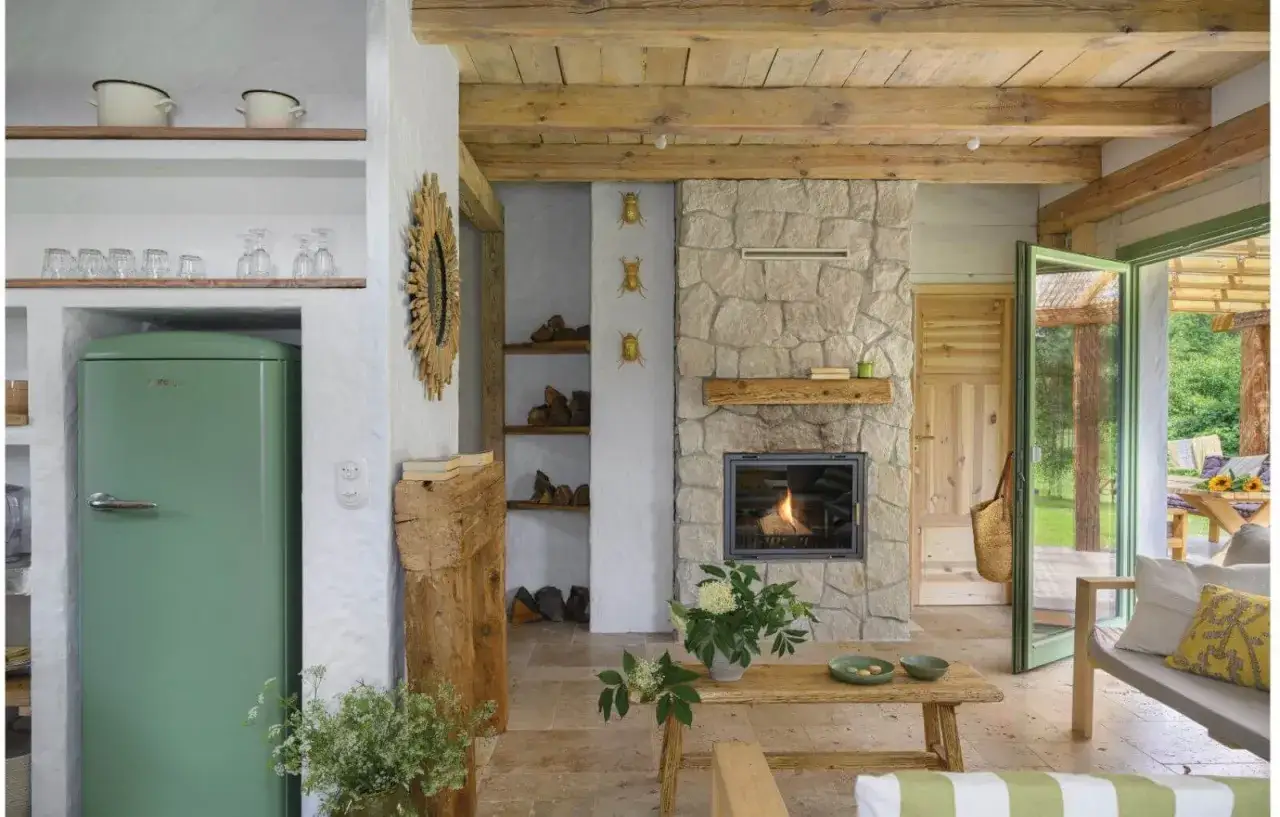 Przytulny salon z kamiennym kominkiem bez zabudowy, zieloną lodówką i drewnianymi belkami na suficie.