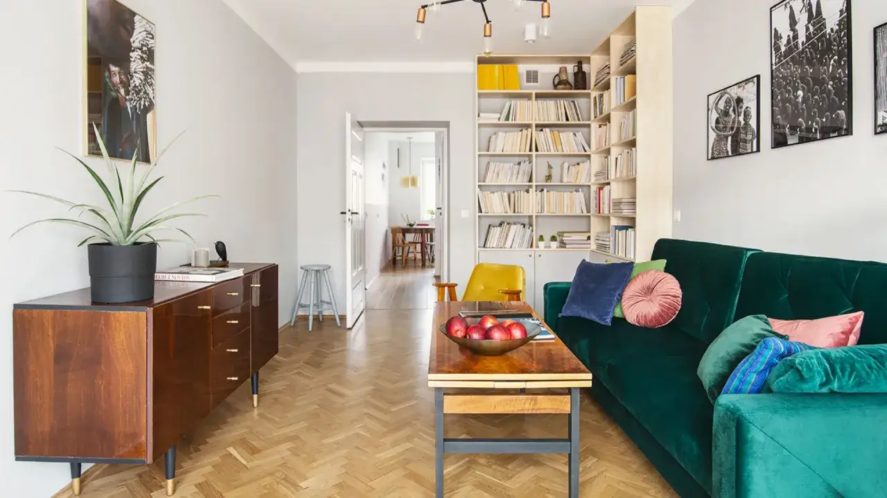 Nowoczesne mieszkanie w stylu PRL z zieloną kanapą, drewnianą komodą i regałem pełnym książek.