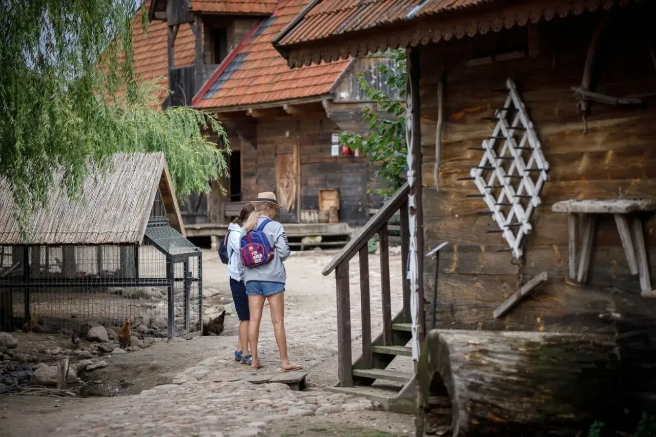 Dwie dziewczyny w słomkowych kapeluszach zwiedzają skansen. Idealne miejsce, gdzie można wykorzystać bon turystyczny bez noclegu na lokalne atrakcje i pamiątki.