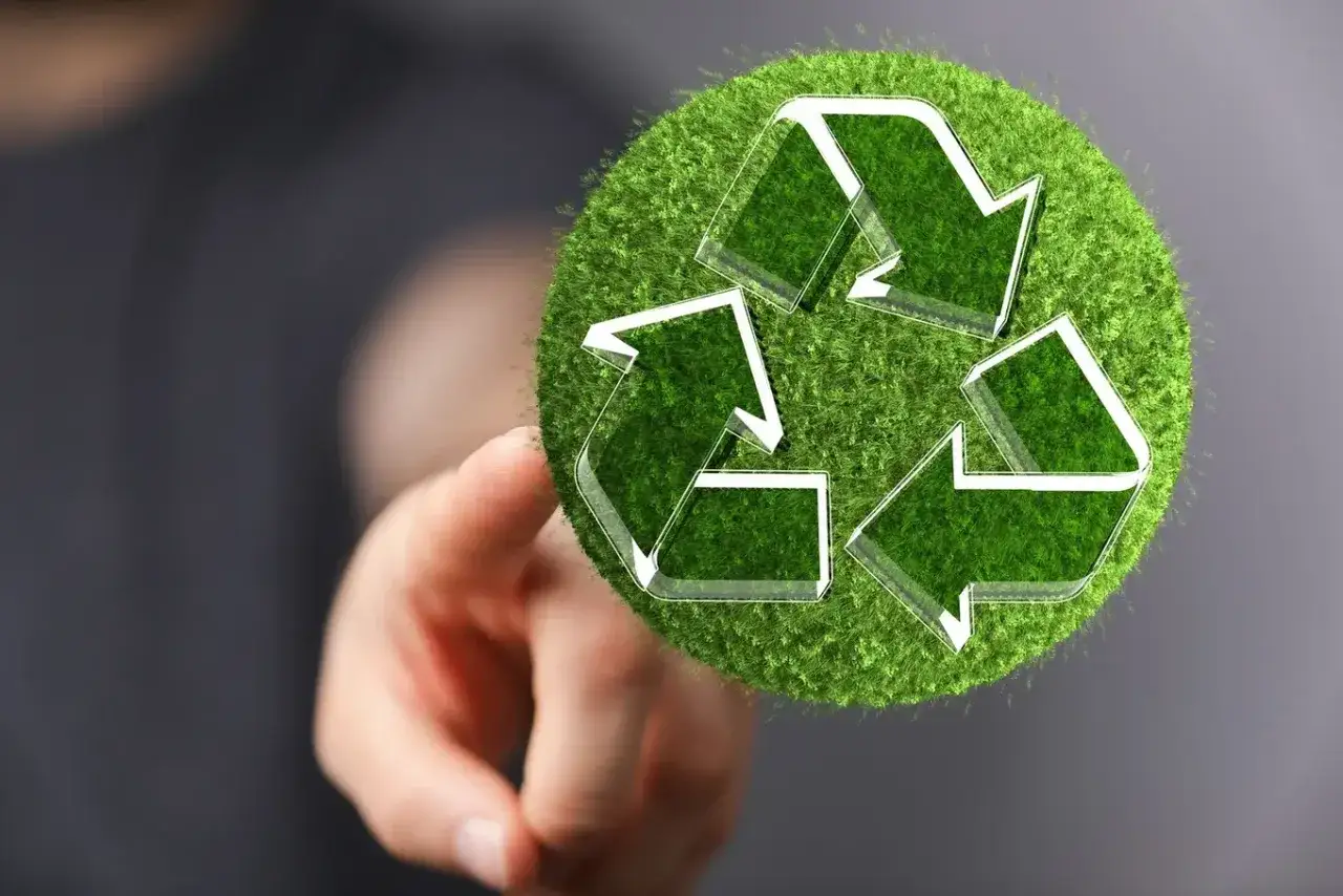 Palec wskazujący dotyka zielonego punktu z symbolem recyklingu.