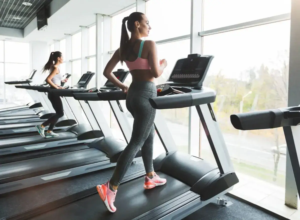 Kobiety ćwiczą na bieżniach, zastanawiając się, czy chodzenie na bieżni odchudza. Trening cardio w nowoczesnej siłowni.