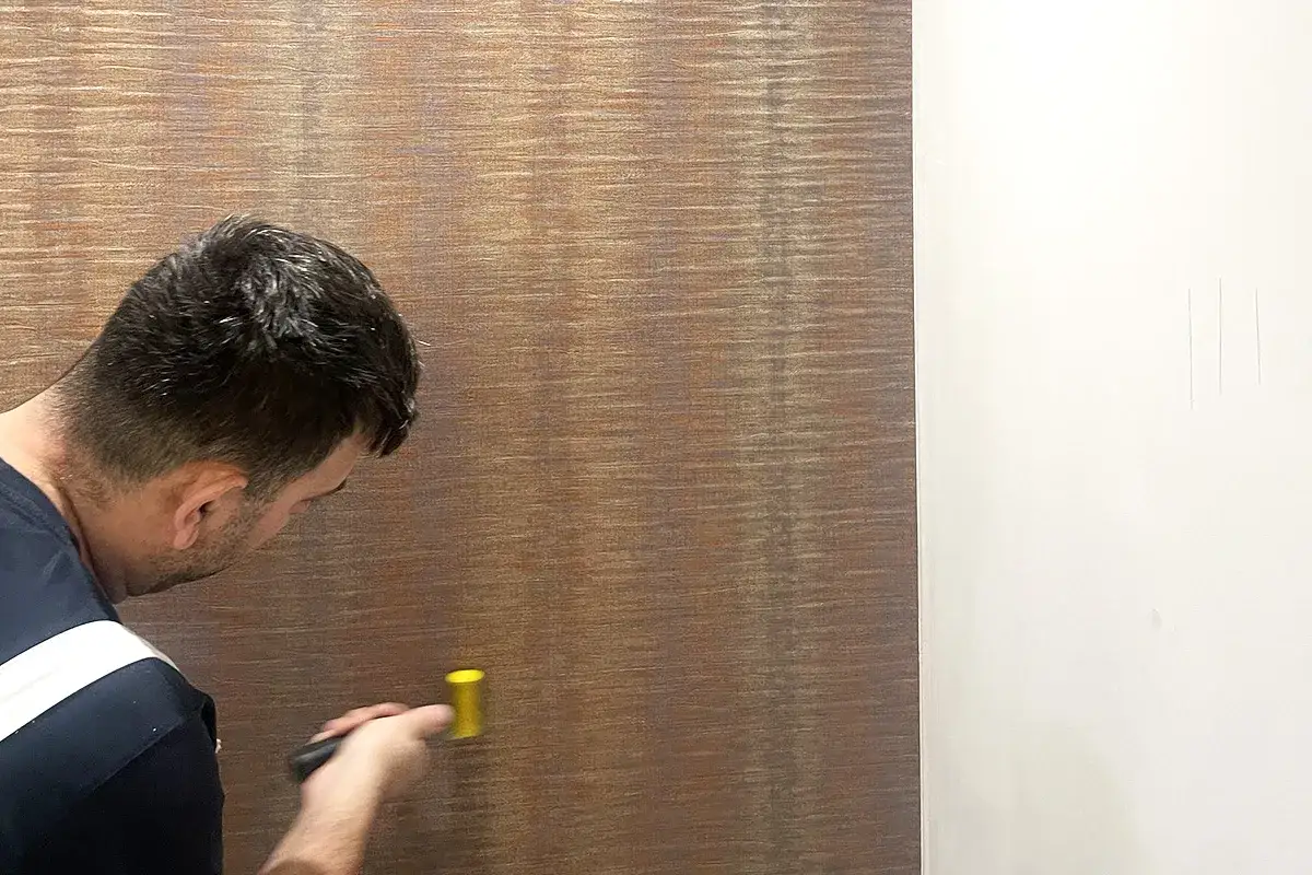 Mężczyzna z wałkiem przygotowuje ścianę pod tapetę, sprawdzając jej gładkość.