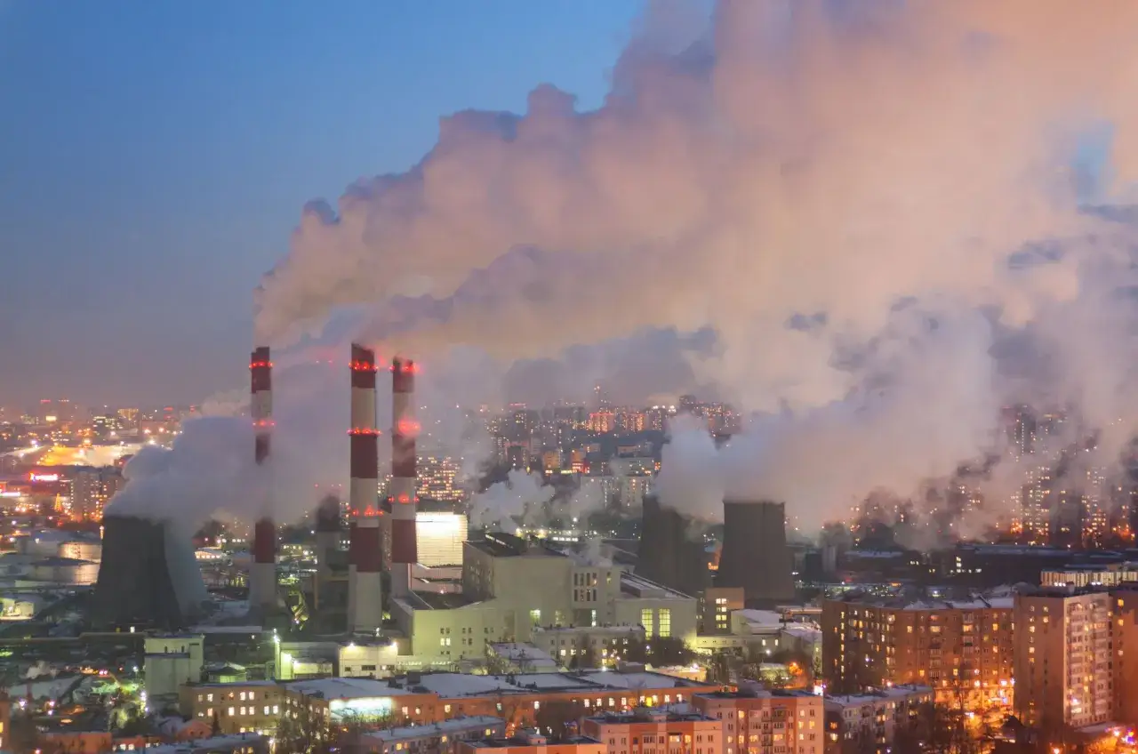 Gęste kłęby pary unoszą się z kominów elektrociepłowni, tworząc mglistą zasłonę nad oświetlonym nocą miastem.