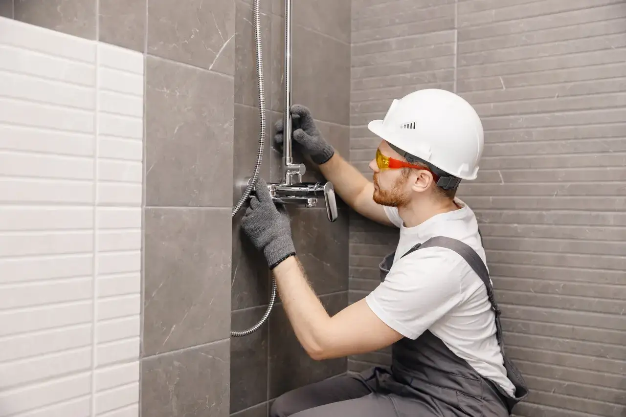 Instalator w kasku i okularach montuje baterię prysznicową. Dowiedz się, ile kosztuje wymiana baterii prysznicowej.
