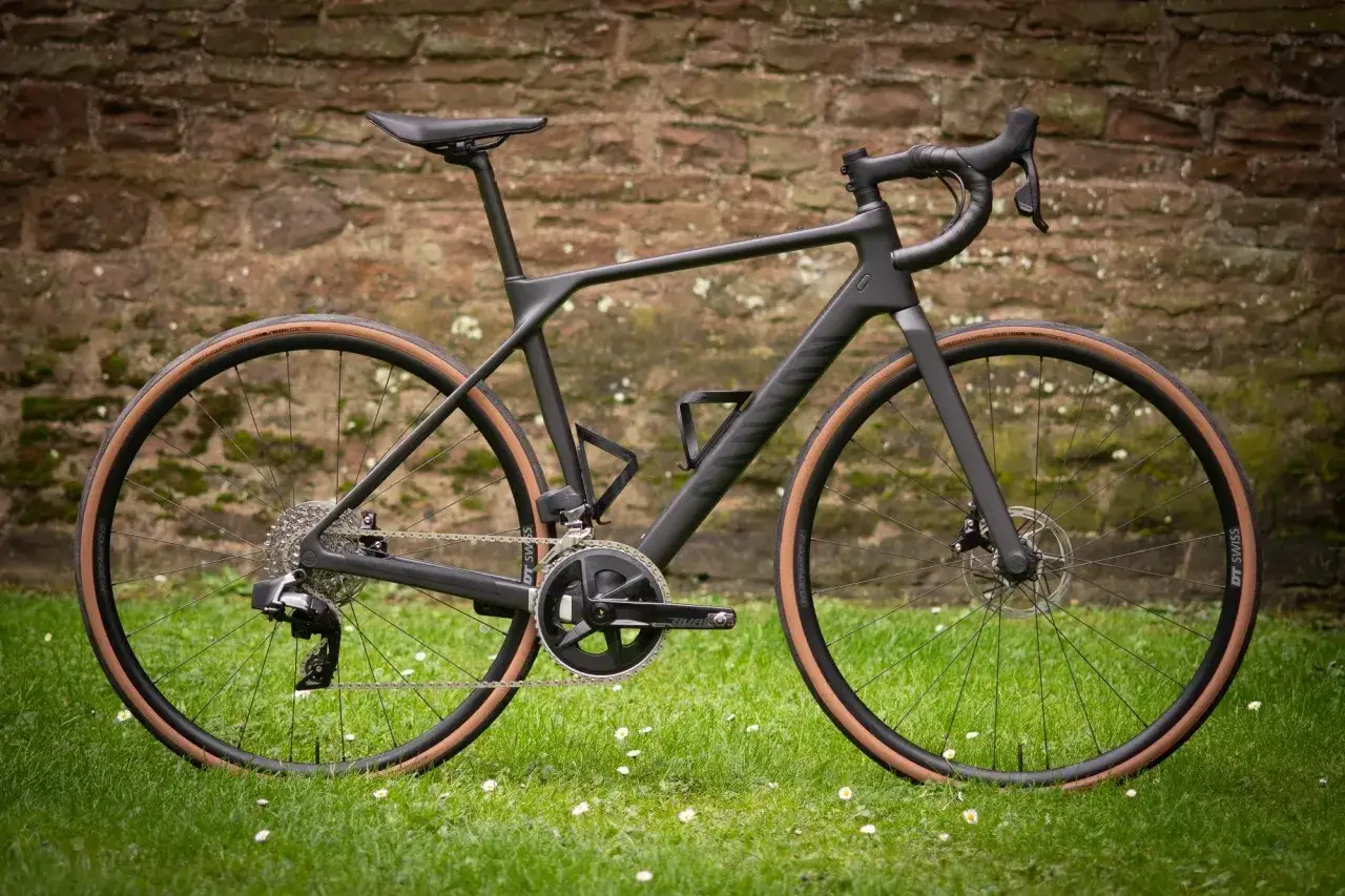Czarny rower szosowy endurance z brązowymi oponami, gotowy na długie trasy pośr&oacute;d zielonej trawy i kamiennego muru.