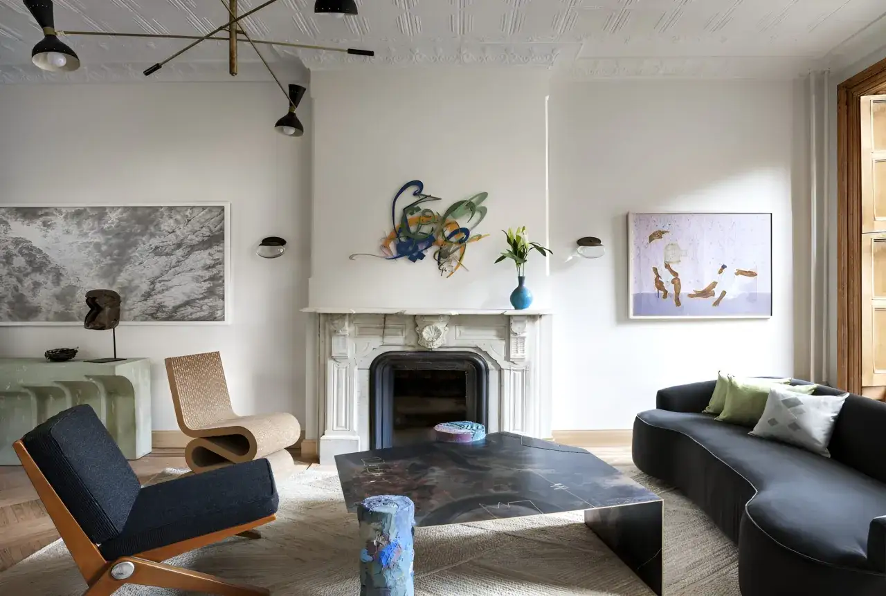 Nowoczesny salon z czarną sofą, designerskimi fotelami i stolikiem kawowym. Wnętrze emanuje dobrym designem, podkreślonym przez sztukę na ścianach.