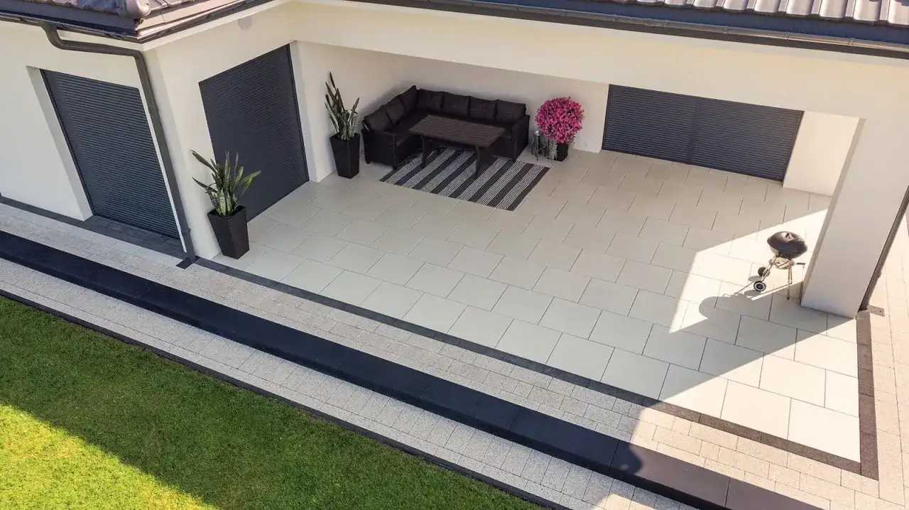 Nowoczesna przestrzeń z sofą i grillem, otoczona opaską wokół domu z płyt chodnikowych.