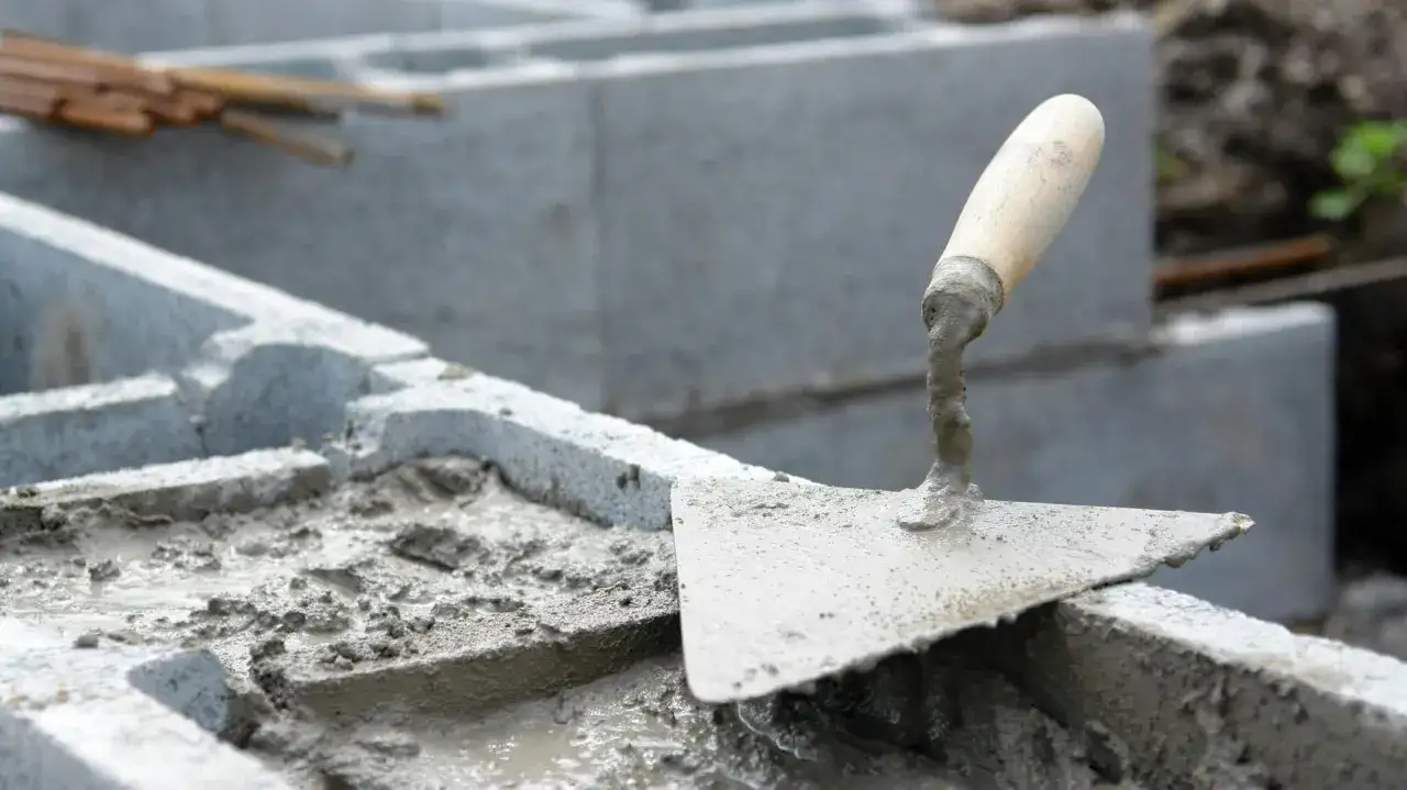 Łopata z zaprawą na budowie, powstaje solidny płot murowany z pustak&oacute;w.