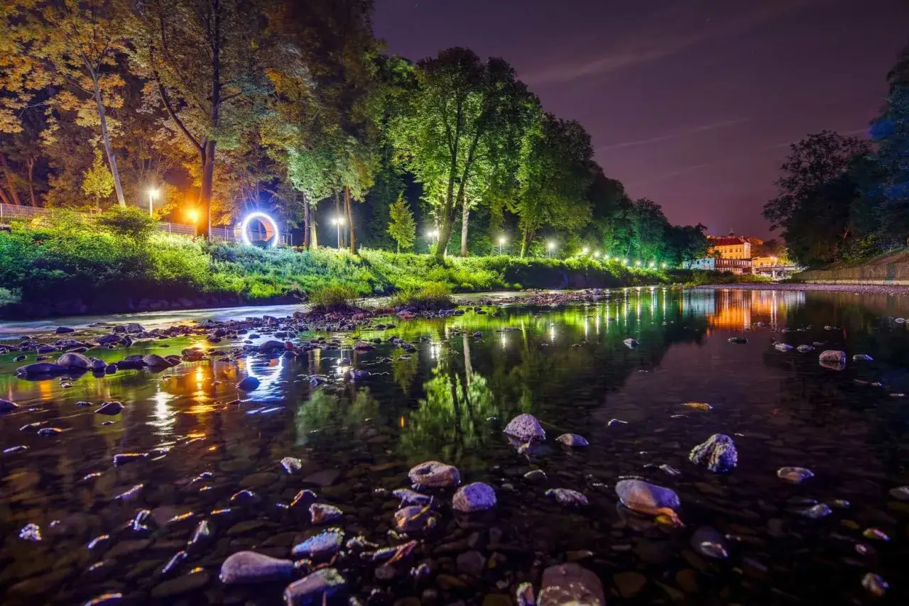 Nocny spacer po Cieszynie: rzeka z kamieniami, oświetlone drzewa i budynek. Idealne miejsce, by zobaczyć magię miasta.