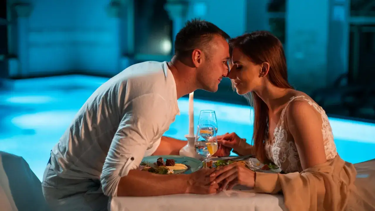 Romantyczna kolacja przy świecach, idealny pomysł na sylwestra we dwoje. Para pochyla się ku sobie, czuć bliskość i miłość.
