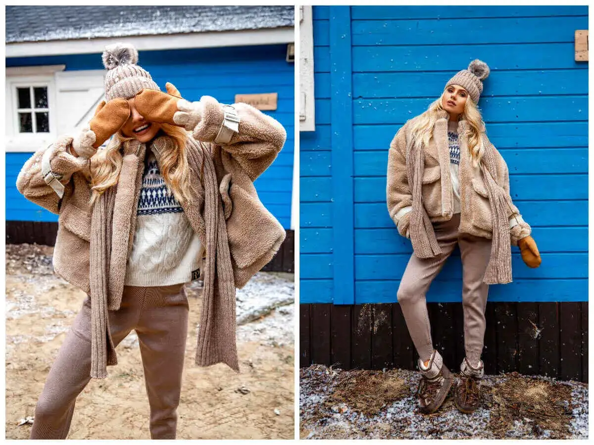 Stylowy outfit na zimę: puchata kurtka, czapka, szalik i rękawiczki w beżowych odcieniach. Modelka pozuje na tle niebieskiego domku.