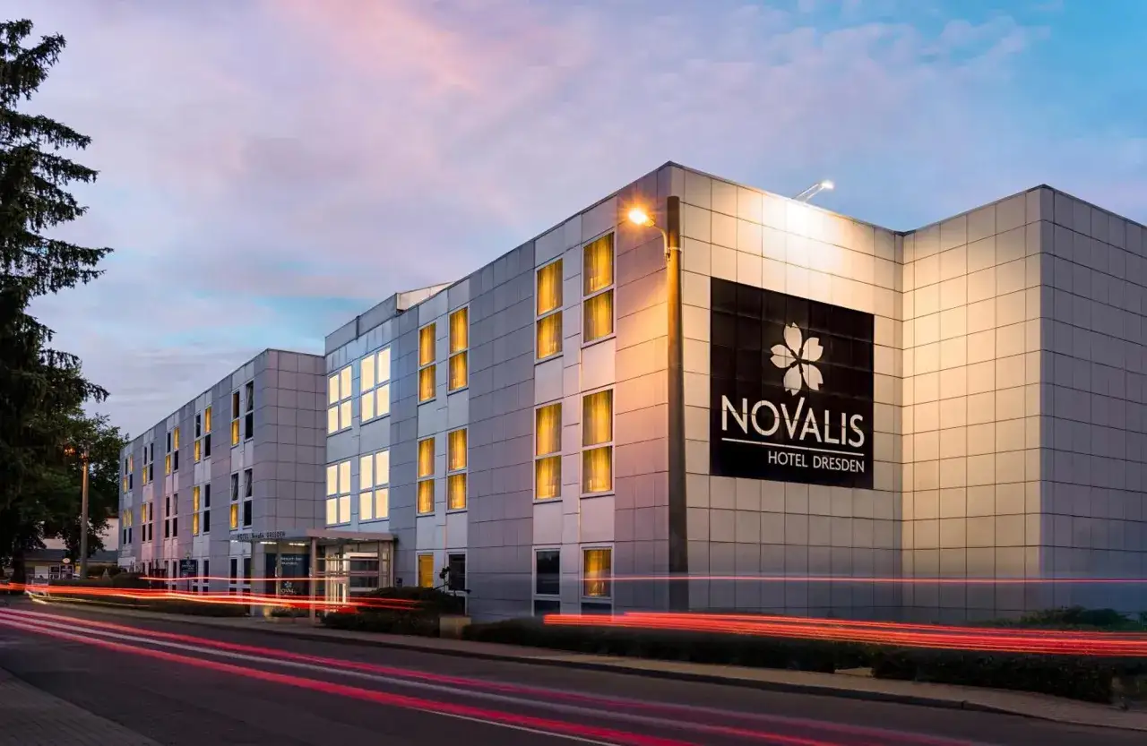 Nowoczesny hotel Novalis w Dreźnie, z oświetlonymi oknami i neonowymi światłami samochodów na drodze.