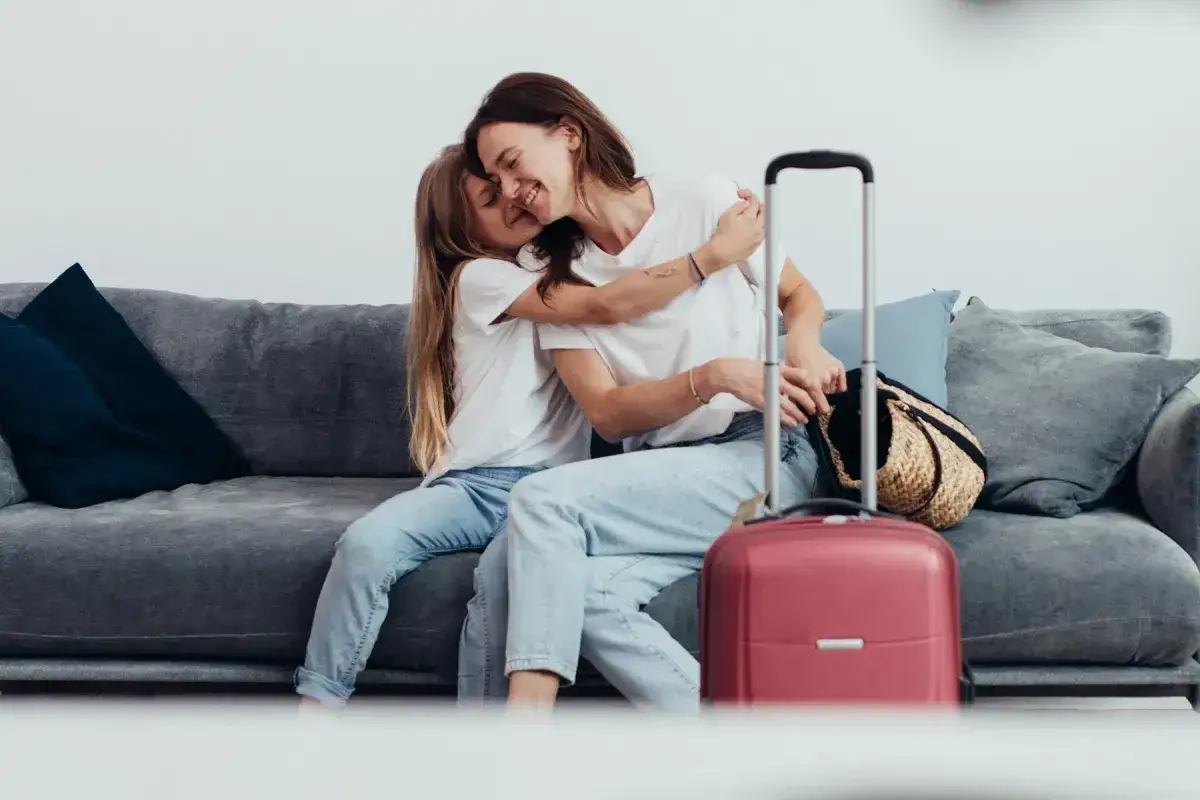 Mama i córka przytulają się na kanapie obok walizki. Ile trzeba mieć lat żeby zameldować się w hotelu? Zazwyczaj 18.