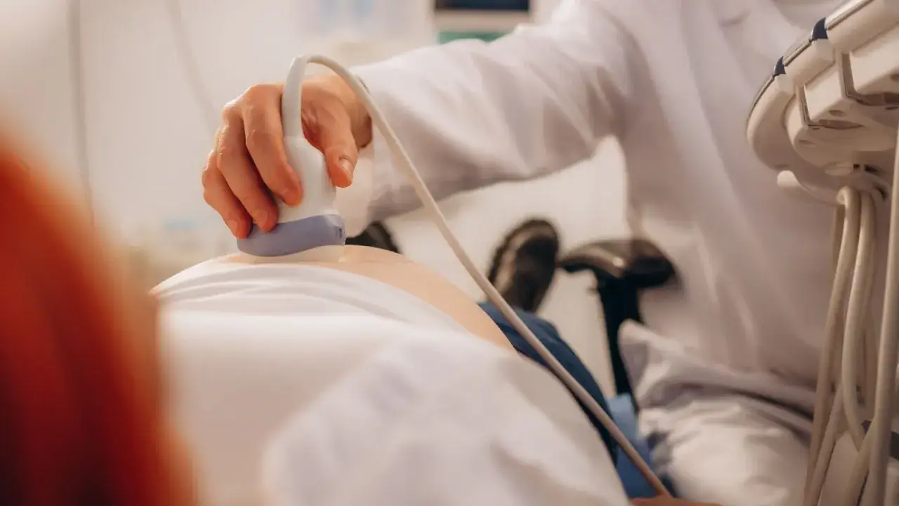 Lekarz wykonuje badania prenatalne NFZ, przykładając głowicę USG do brzucha pacjentki.