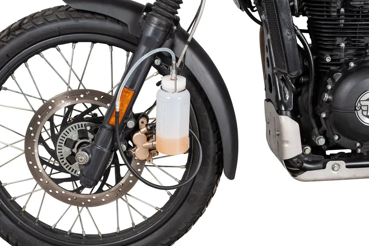 Zestaw do odpowietrzania hamulc&oacute;w z ABS w motocyklu. Przezroczysty zbiorniczek z płynem podłączony do zacisku hamulcowego.
