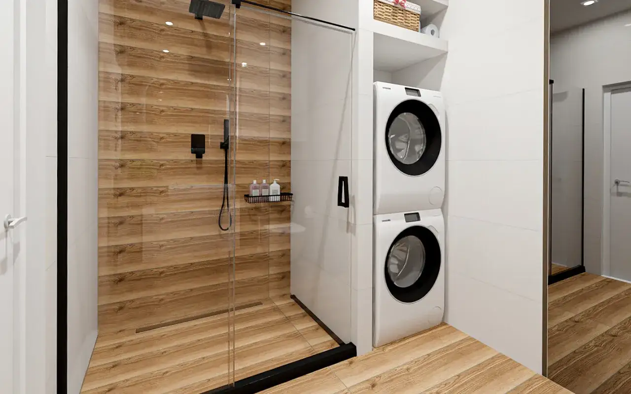 Bardzo mała łazienka z prysznicem i pralką ustawioną jedna na drugiej. Drewnopodobne płytki na ścianie prysznica i podłodze.