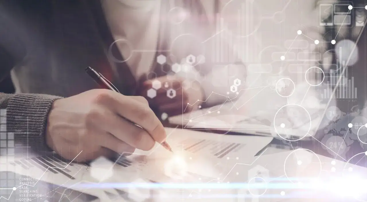 Ręka pisząca na dokumentach, otoczona cyfrowymi wykresami i danymi. Tak wygląda staż w nowoczesnej firmie, pełen analiz i nowych wyzwań.