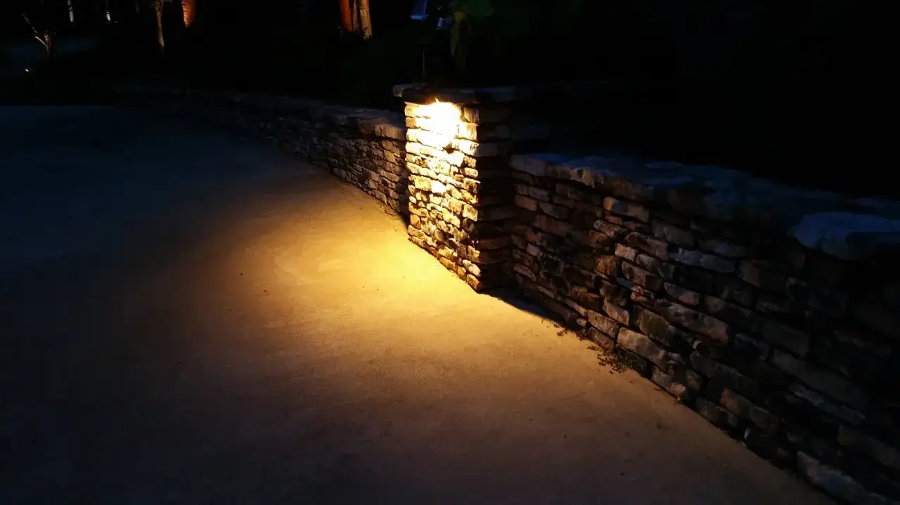 Ciepłe oświetlenie ściany z kamienia tworzy przytulną atmosferę przy ścieżce.