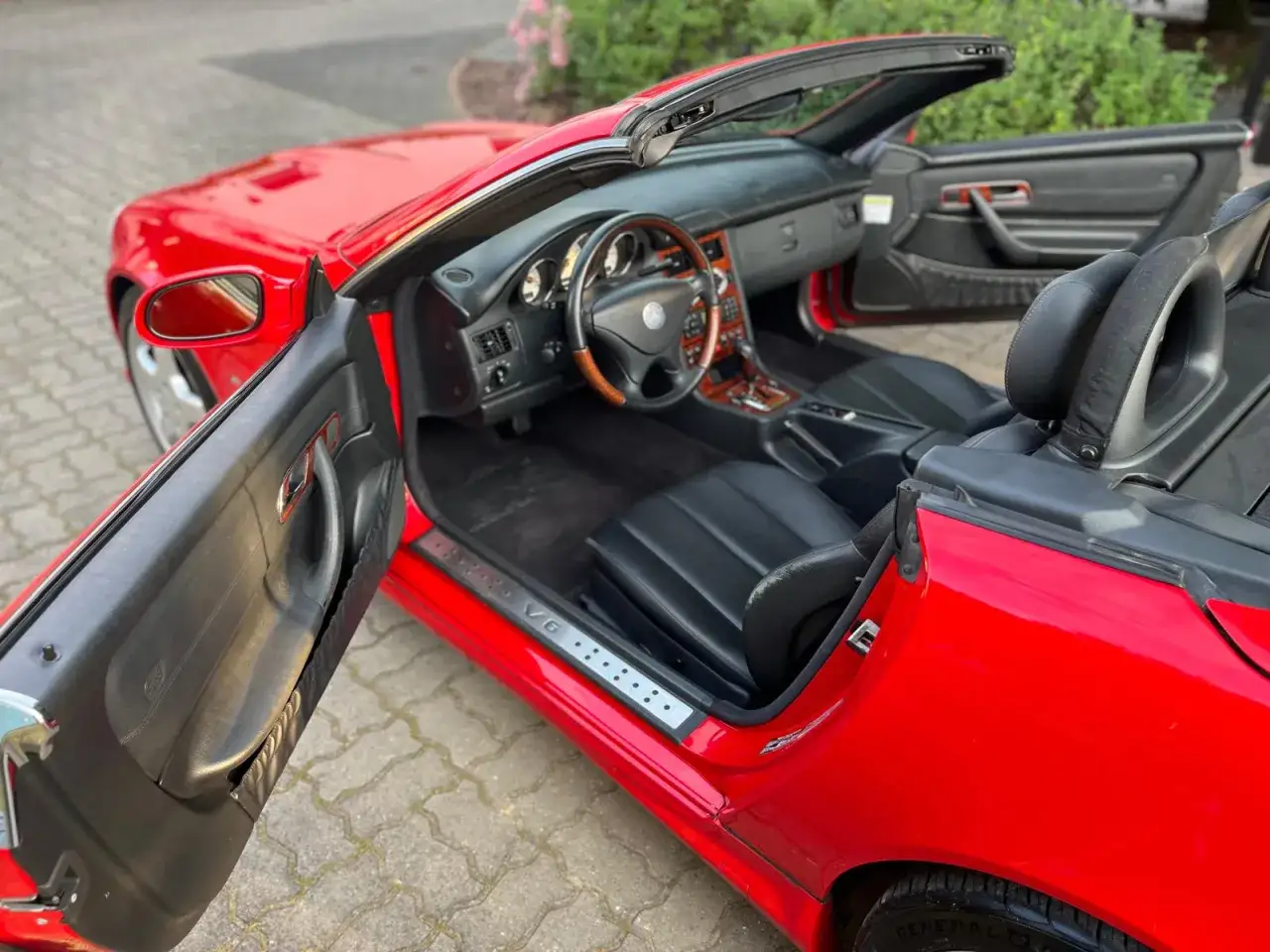 Czerwony Mercedes Benz SLK z otwartymi drzwiami, widoczne czarne skórzane fotele i drewniane wykończenie deski rozdzielczej.
