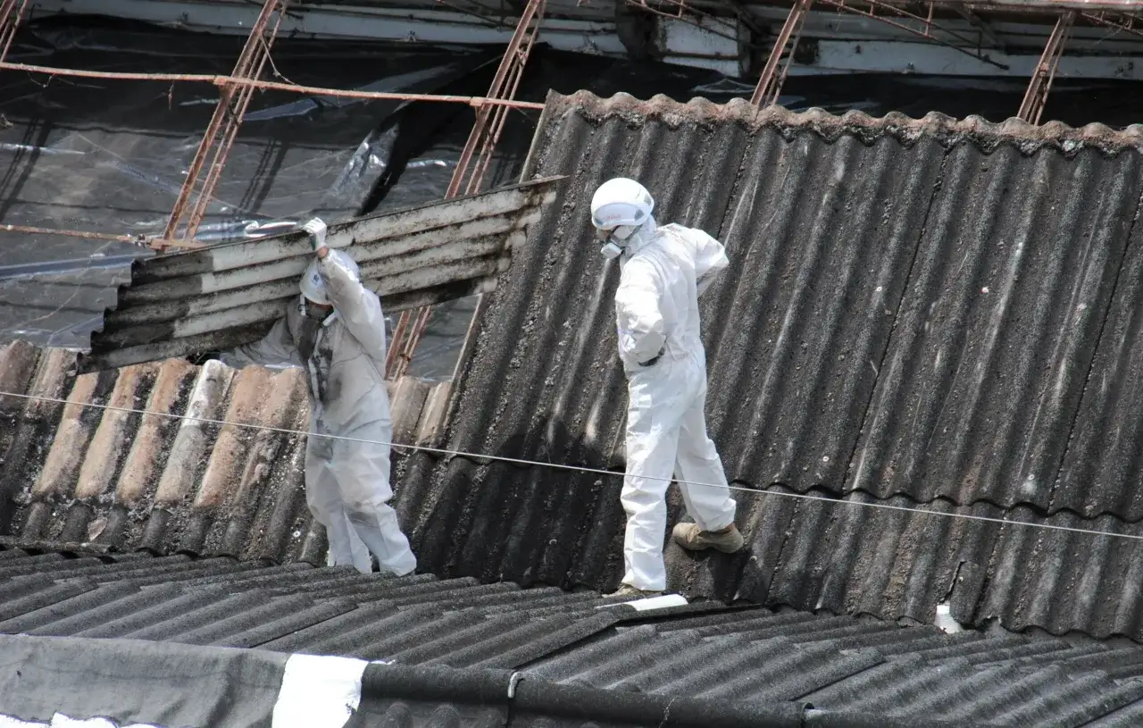 Pracownicy w kombinezonach usuwają eternit. Koszt azbestu jest wysoki ze względu na zagrożenie dla zdrowia.