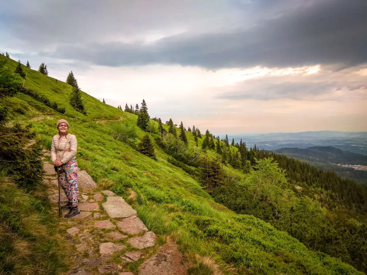 Kobieta na kamiennym szlaku w g&oacute;rach, otoczona zielenią i drzewami. Czy to właśnie ten szlak na Śnieżkę najłatwiejszy?