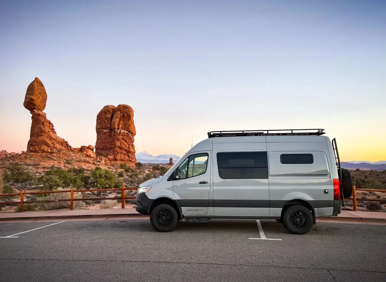 Szary kamper VanSmith na tle skalnych formacji w Arches National Park. Idealny na wypożyczenie i niezapomnianą podr&oacute;ż.