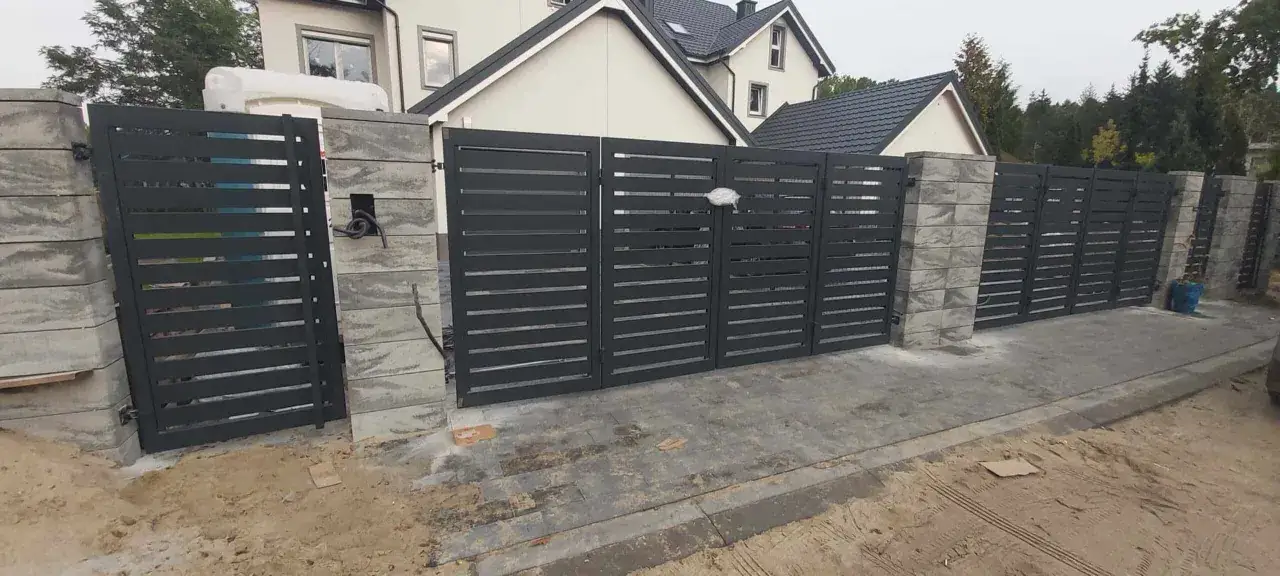 Nowoczesna brama łamana, jak zrobić taką? Szare, metalowe przęsła z betonowymi słupkami, idealne do nowoczesnego domu.