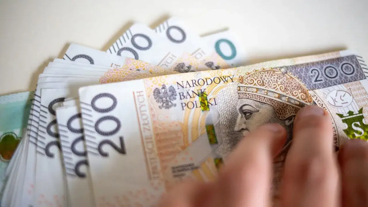 Dłoń przesuwa stos banknotów 200 zł. Czy emeryta obowiązuje okres wypowiedzenia? Pieniądze to ważna sprawa.