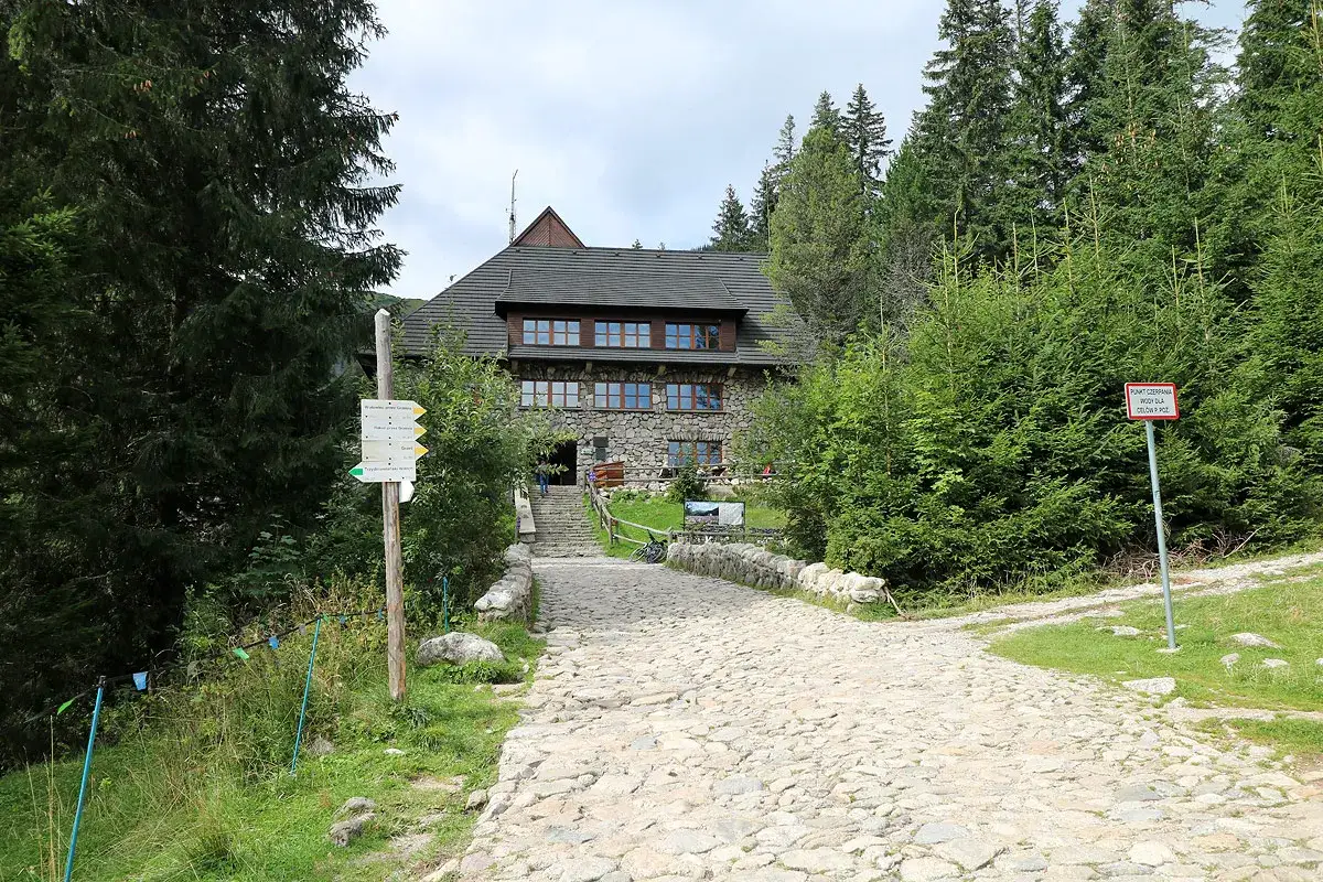 Kamienista ścieżka prowadzi do kamiennego schroniska w dolinie wyżniej Chochołowskiej, otoczonego gęstym lasem świerkowym.